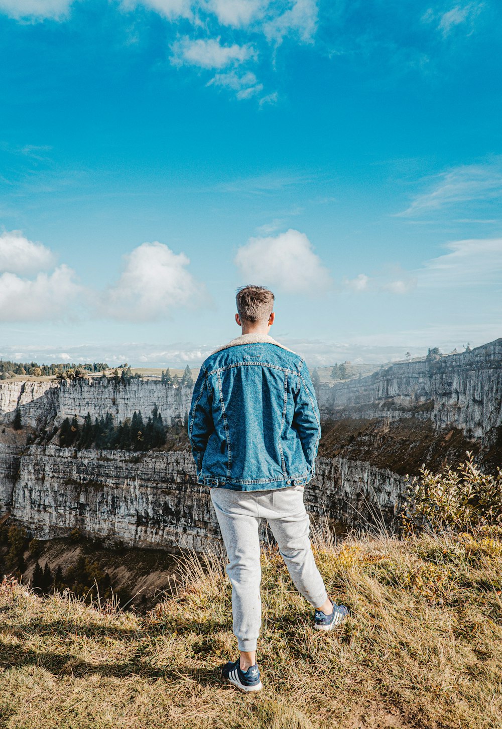 man in blue dress shirt standing on cliff during daytime