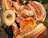 Colorful traditional dancers, wearing vibrant orange dresses adorned with multicolored stripes and ruffles, perform energetically. One dancer holds her dress out gracefully, while another wears a wide-brimmed hat and detailed black attire.
