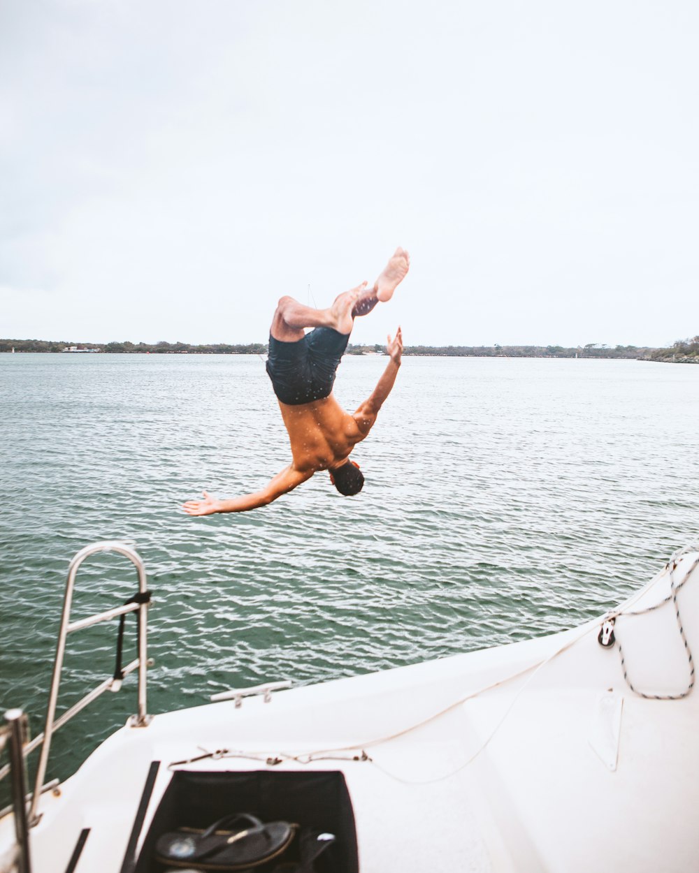 homem de shorts pretos pulando no barco branco durante o dia
