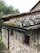 Old stone building with a weathered roof covered in moss and lichen. The structure features a mix of bricks and stones with a rustic appearance. Metal gutters and downspouts are attached to the roof.