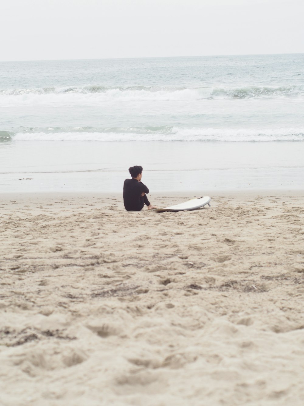 Mann im schwarzen Neoprenanzug, der tagsüber weißes Surfbrett am Strand hält