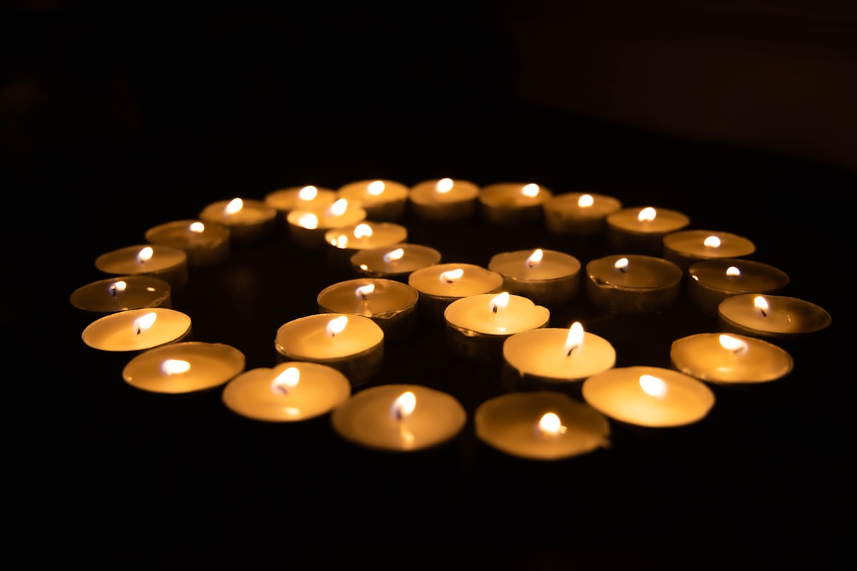 Tea Candles arranged like a peace sign.  They have a warm orange glow and are against a black background.