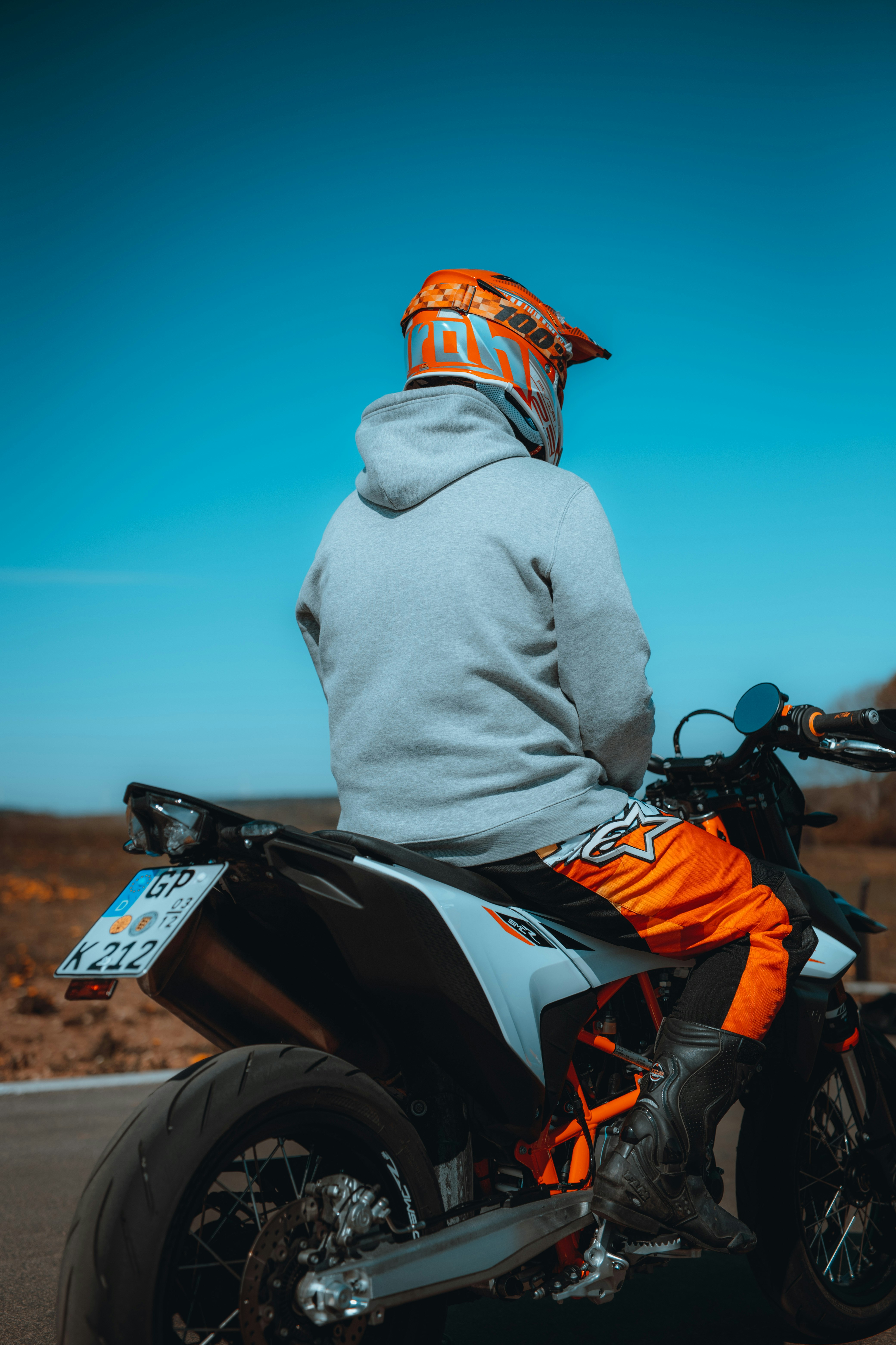 man in gray hoodie riding orange and black motorcycle