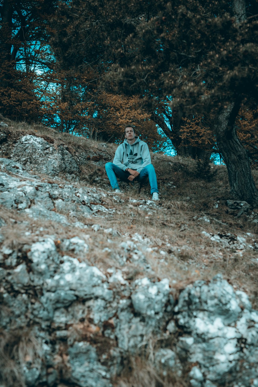 hombre con sudadera con capucha gris sentado en roca gris