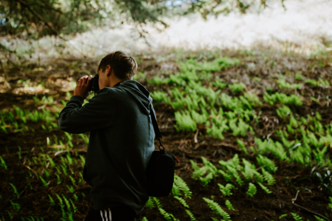 man in black hoodie taking photo of green grass during daytime