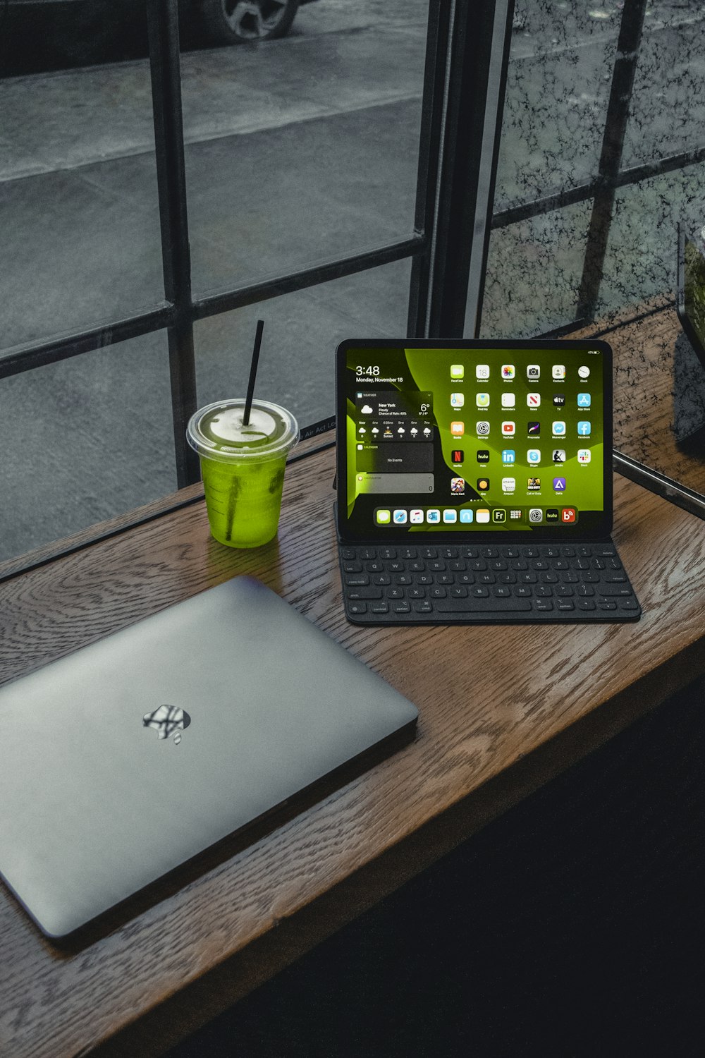 macbook pro beside green plastic cup on brown wooden table