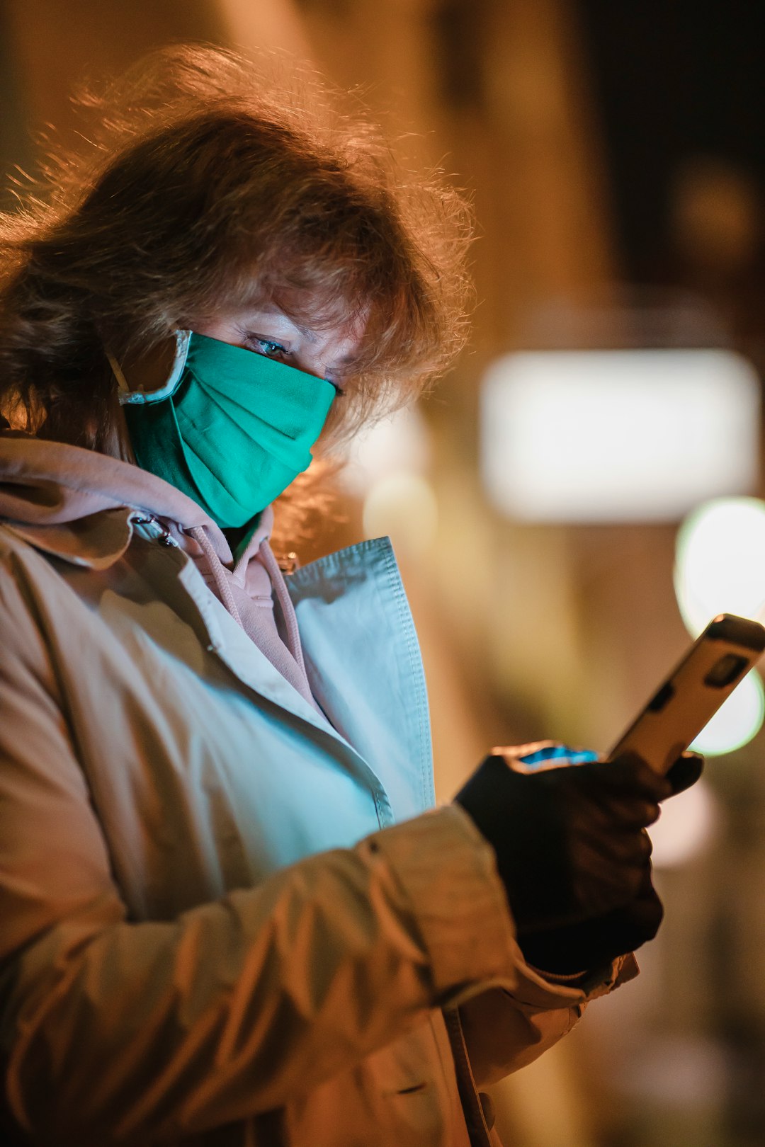 Woman in green face mask using smartphone at night during the COVID-19 pandemy. Warsaw, Old Town, Poland