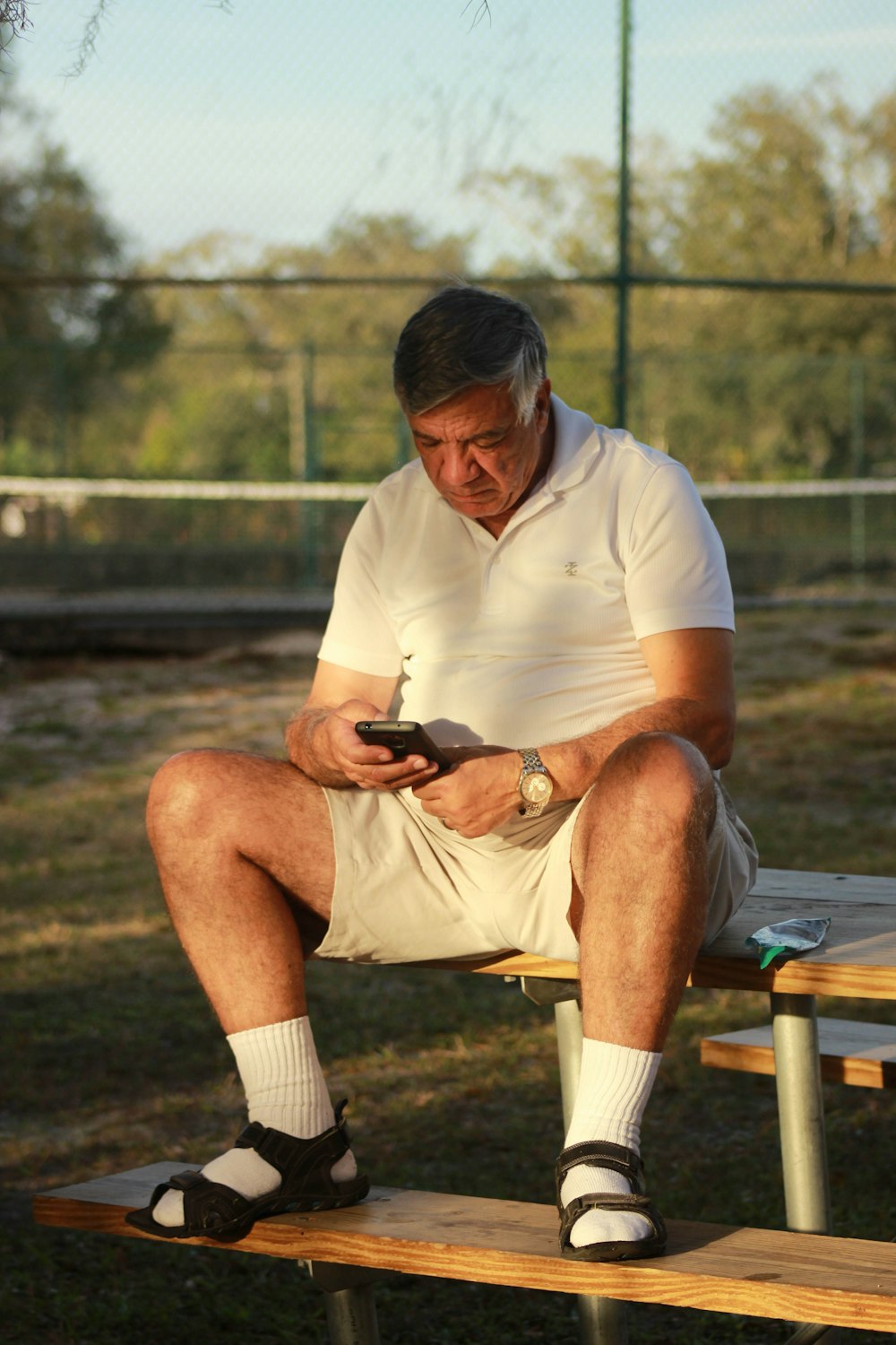 man in white polo shirt and black shorts sitting on brown wooden bench