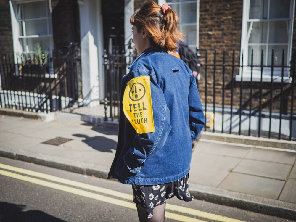 woman in blue jacket walking on sidewalk during daytime