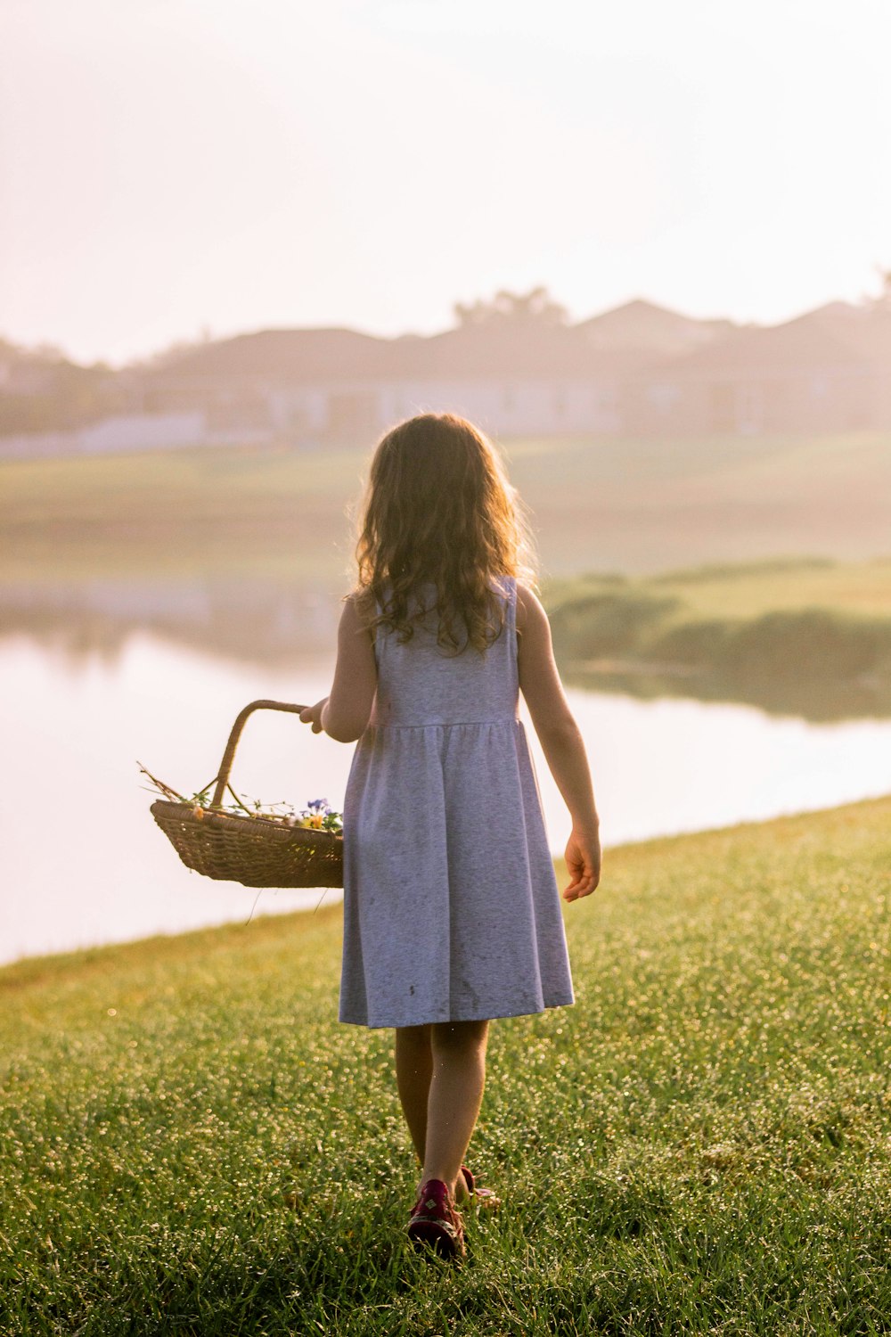 girl in white dress holding brown woven basket walking on green grass field during daytime