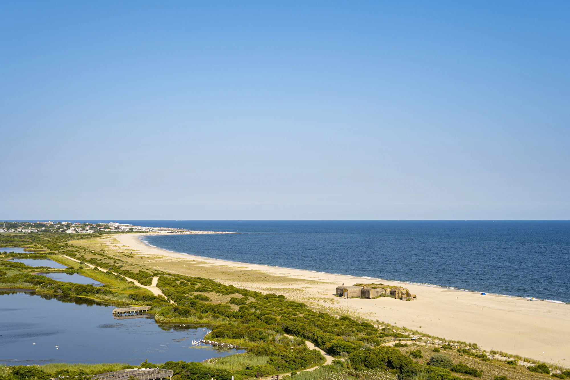 A long sandy barrier beach separates calm marsh ponds from the open blue ocean along the coast.