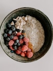 A bowl filled with creamy oatmeal, topped with fresh raspberries, blueberries, and cashew nuts. The ingredients are neatly arranged, creating an appetizing and colorful display.