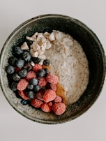 A bowl filled with creamy oatmeal, topped with fresh raspberries, blueberries, and cashew nuts. The ingredients are neatly arranged, creating an appetizing and colorful display.
