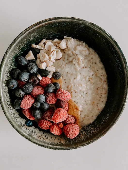 Close-up of a rustic bowl filled with creamy oat porridge topped with fresh berries and a drizzle of honey.