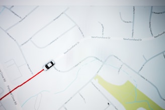 A map with street names and a small black and white car icon following a red path. The map features roads, labels, and a section of yellow indicating a park or green area.