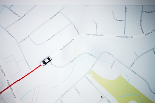 A map with street names and a small black and white car icon following a red path. The map features roads, labels, and a section of yellow indicating a park or green area.