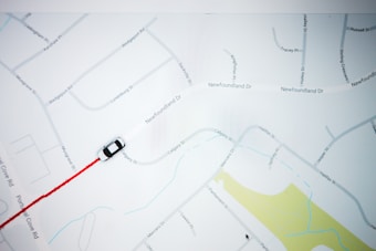 A map with street names and a small black and white car icon following a red path. The map features roads, labels, and a section of yellow indicating a park or green area.