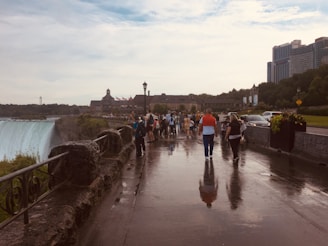 A group of happy tourists walking along the Niagara Falls promenade with the mist rising in the background.
