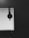 A black and white photograph features a computer monitor displaying a software interface, likely related to graphic design. A pair of over-ear headphones is hanging from the top corner of the monitor. The room appears dimly lit, and the overall setup conveys a workspace.