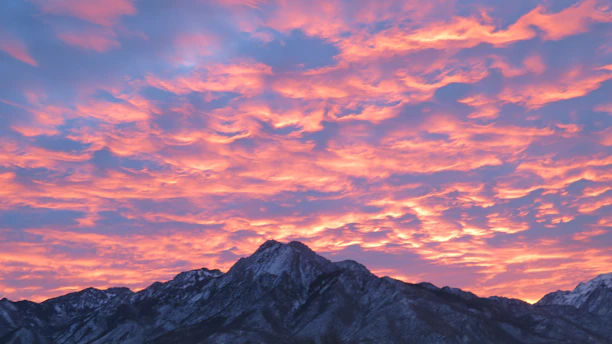 A vibrant sunset over Alaska's rugged mountains, with a photographer capturing the moment.