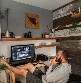 man in gray shirt and black shorts sitting on chair using laptop computer