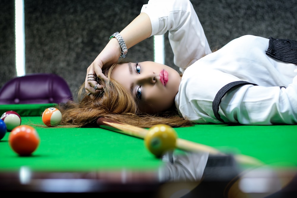 woman in white long sleeve shirt lying on billiard table