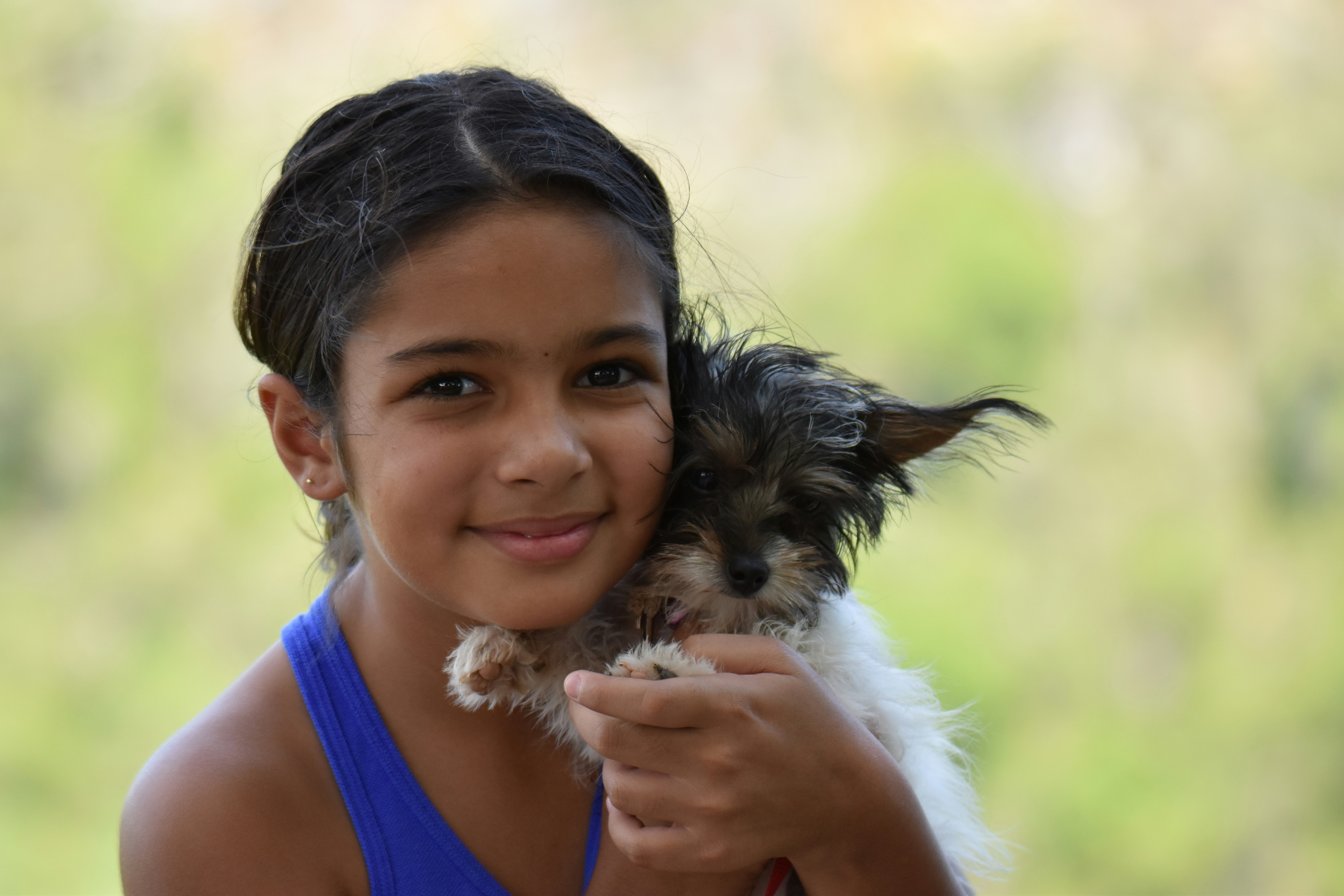 Little girl hugging a fluffy puppy while smiling brightly at a superhero boy standing nearby