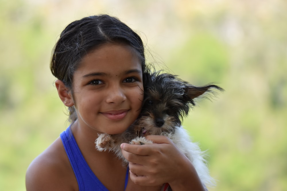 girl in blue tank top holding black and brown long coated small dog