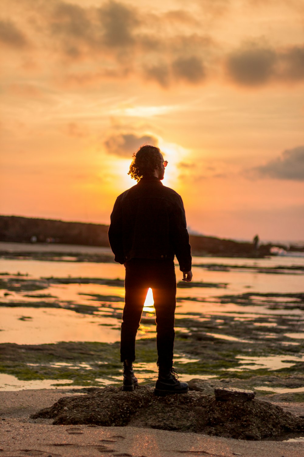 man in black jacket standing on seashore during sunset