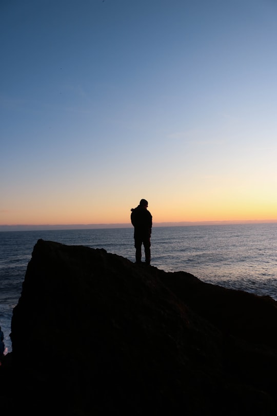 silhouette of man standing on rock formation near body of water during sunset in Vik Iceland