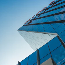 An aerial shot of a modern glass building reflecting a clear blue sky, emphasizing structural clarity and light.