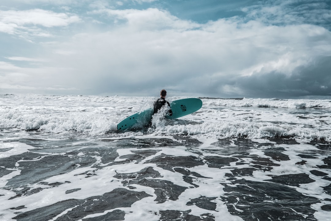 man in green wet suit holding blue surfboard on sea waves during daytime