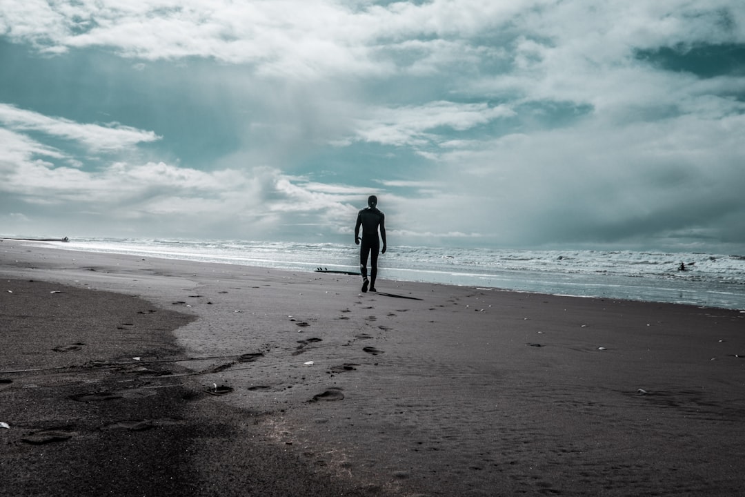 man in black jacket walking on beach during daytime