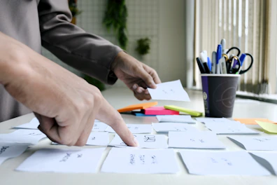 A person pointing at a sticky note on a desk during a brainstorming session