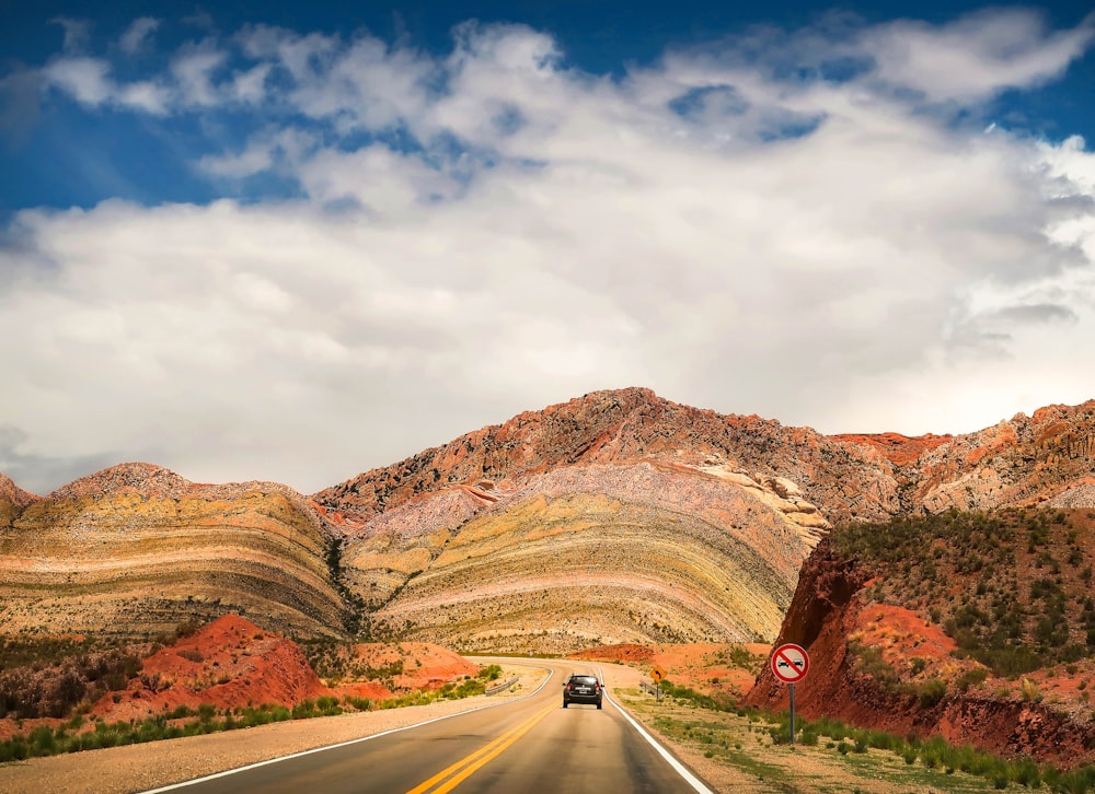 gray asphalt road between brown mountains under white clouds and blue sky during daytime