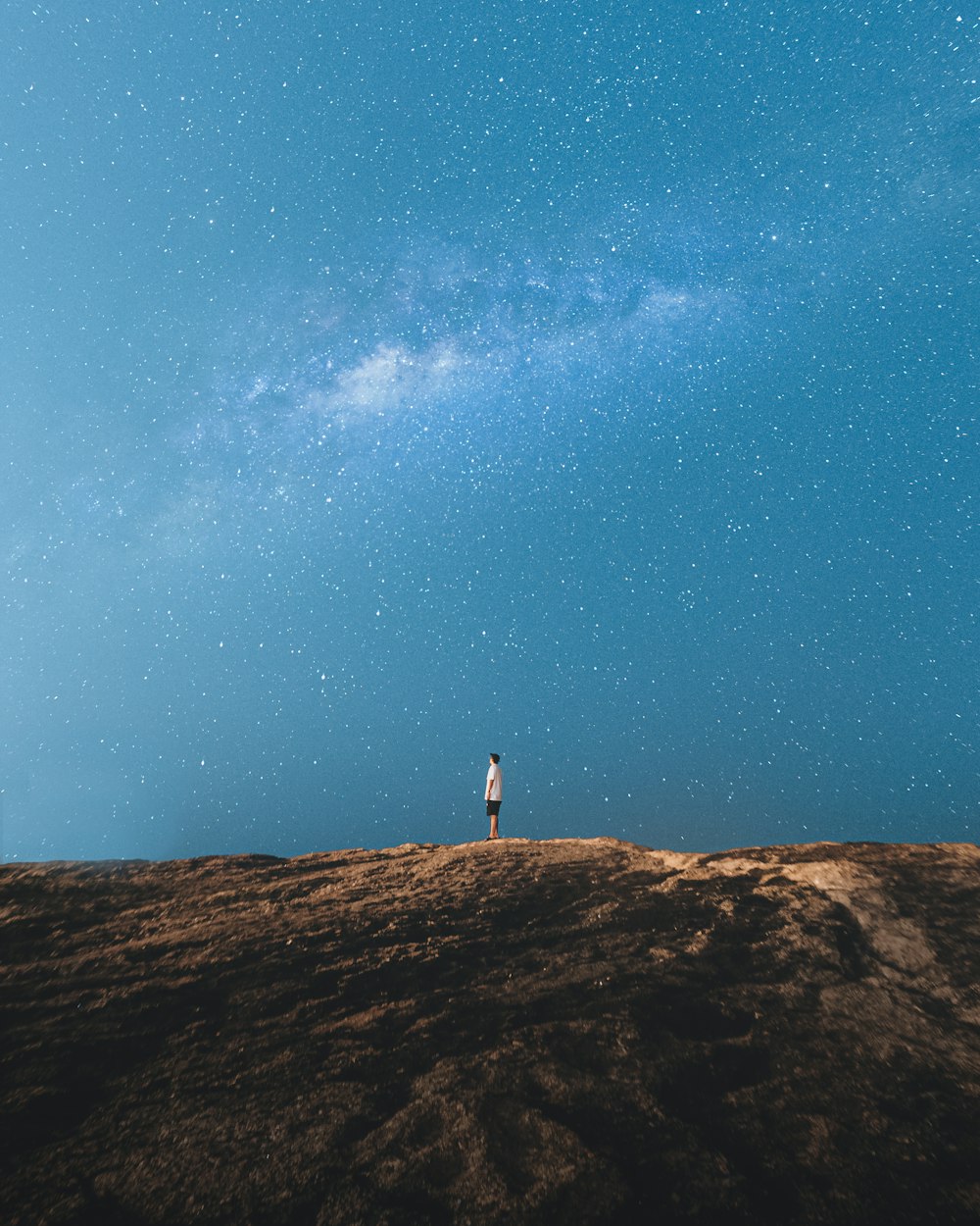 Persona in piedi su roccia marrone sotto cielo blu durante il giorno