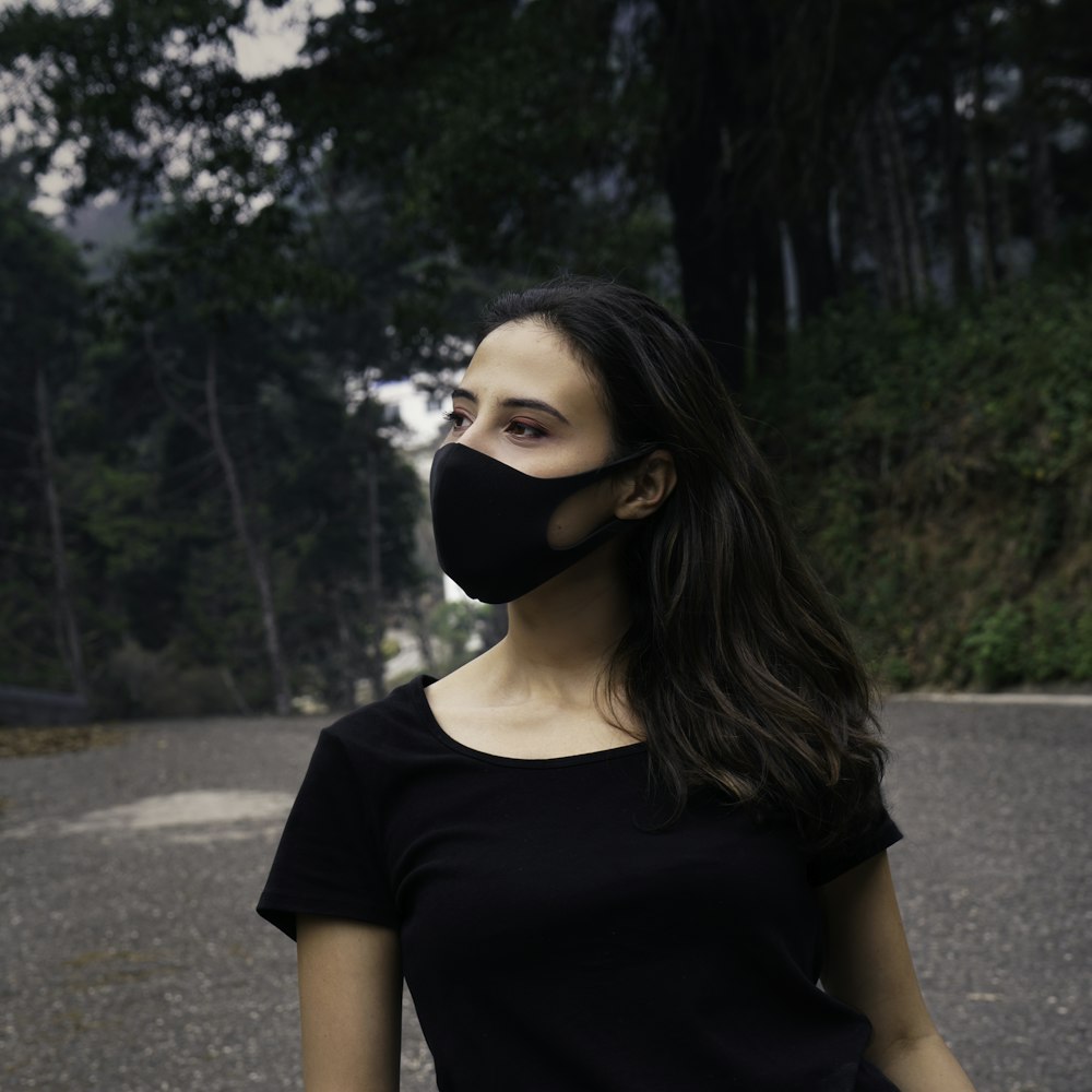 woman in black crew neck t-shirt wearing black mask standing on road during daytime