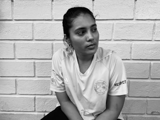 A person wearing a sports jersey sits against a brick wall, looking contemplative. The jersey displays logos and the word 'RESPECT' on the sleeve.