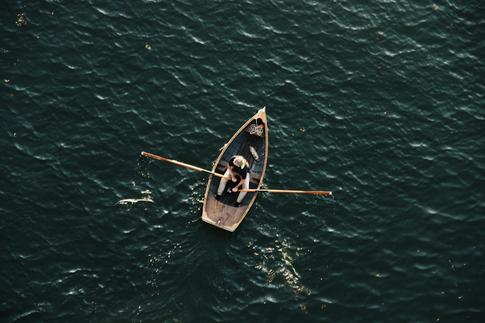 man in black shirt riding on brown wooden boat on green sea during daytime