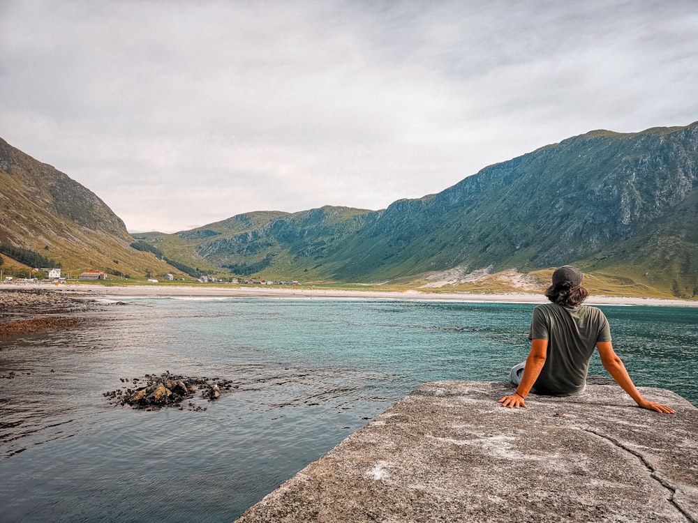 man in black t-shirt sitting on rock near body of water during daytime