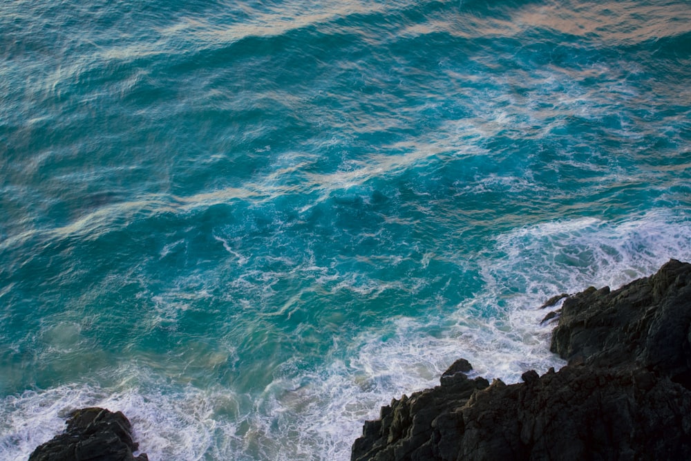 blaue Meereswellen, die tagsüber auf schwarze Felsformationen stürzen