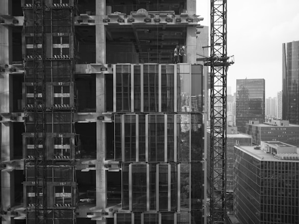 Modern high-rise building under construction with workers and cranes.