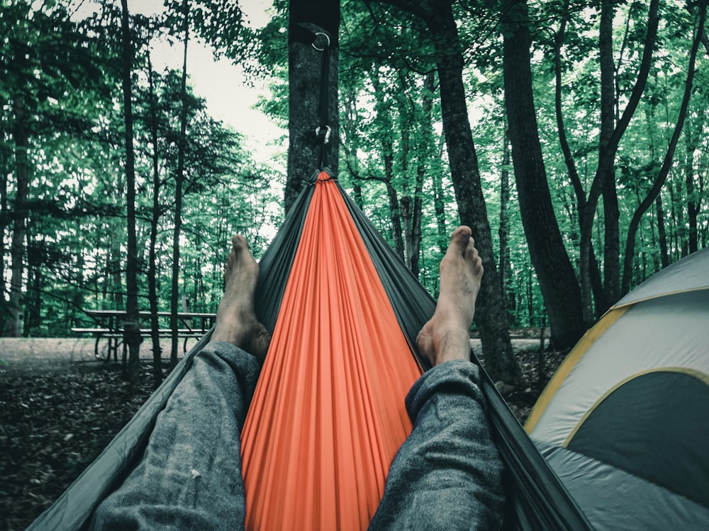 person in black pants lying on orange hammock