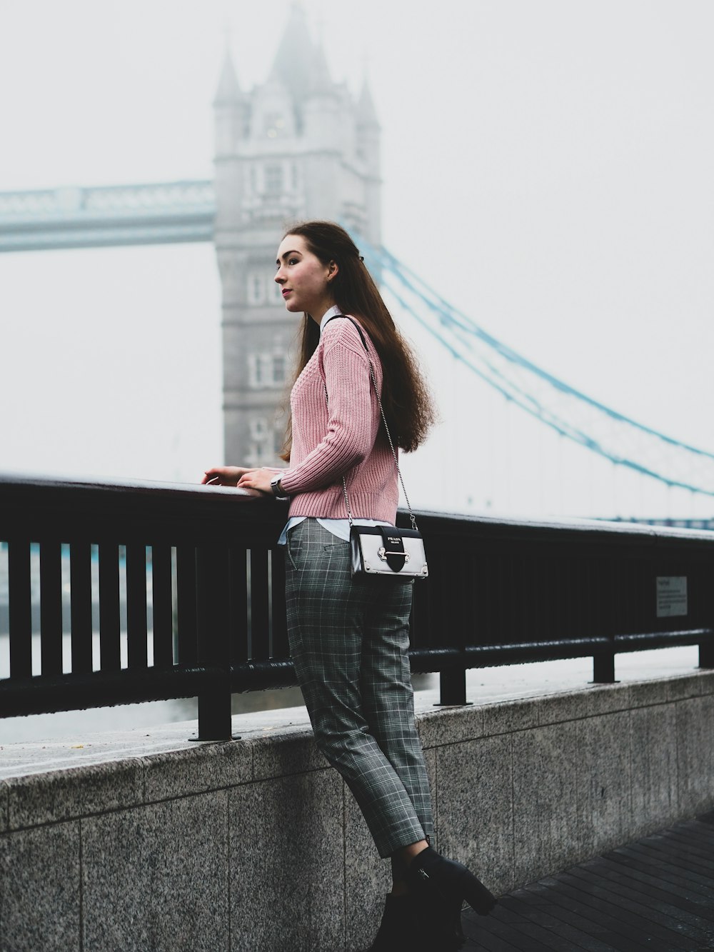 woman in pink long sleeve shirt and blue denim jeans standing on bridge during daytime