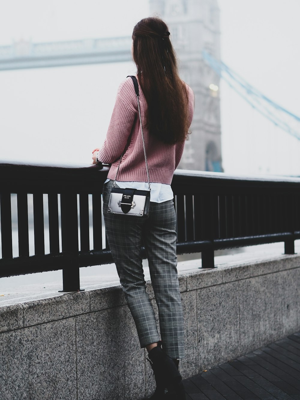 woman in red sweater and blue denim jeans standing on gray concrete bridge during daytime