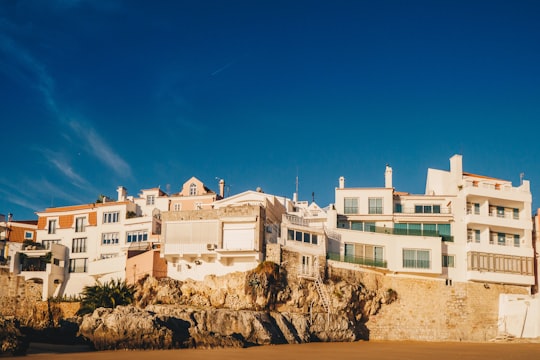 white concrete building on brown rock formation under blue sky during daytime in Cascais Portugal