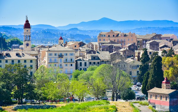 White and brown concrete building near green trees and mountain during daytime — Corfu, Greece