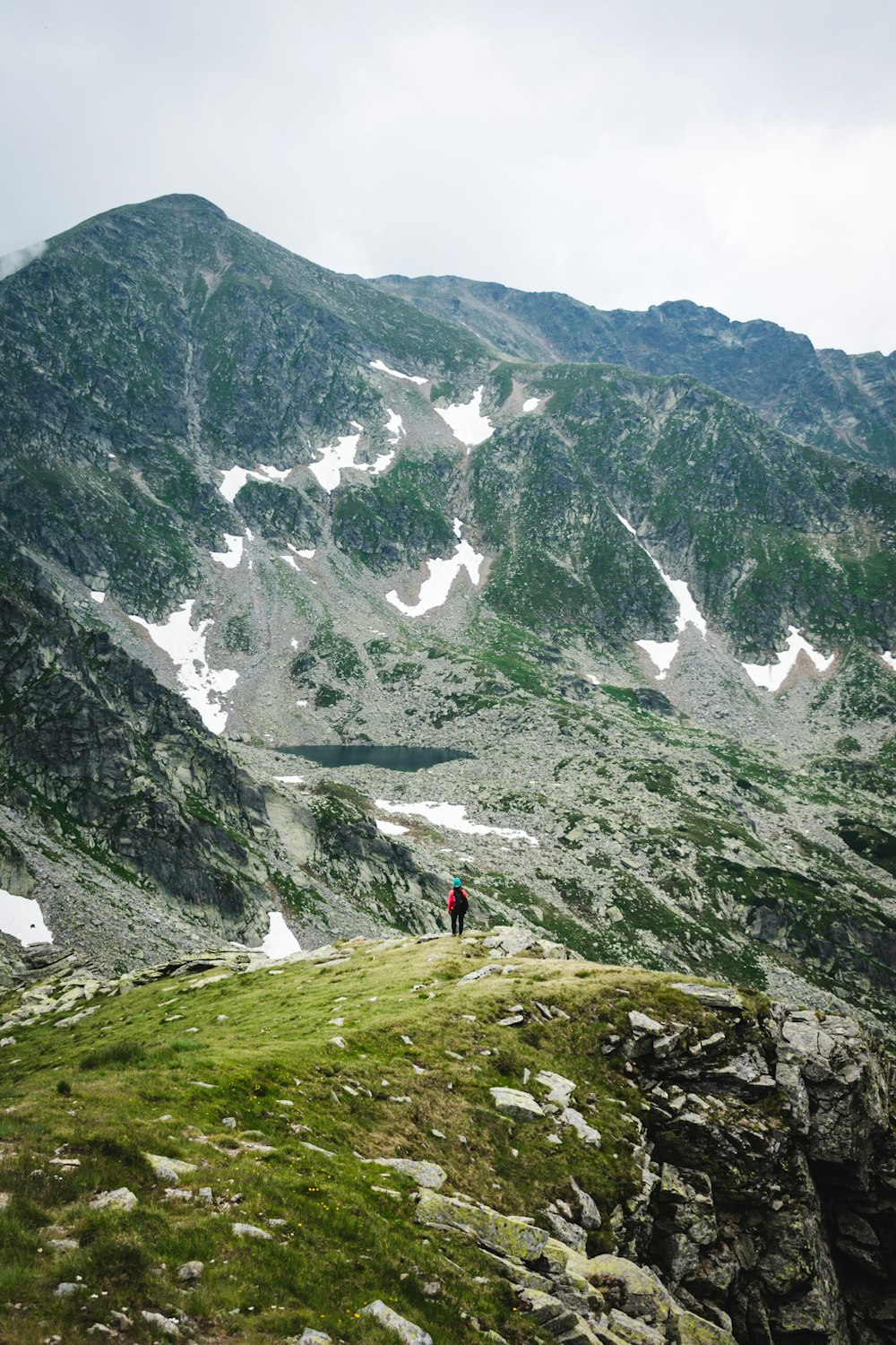 person in red jacket standing on green grass field near gray mountain during daytime