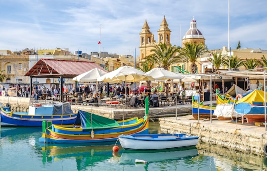 blue and yellow boat on water near brown concrete building during daytime in Marsaxlokk Parish Church Malta