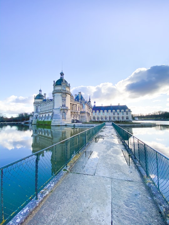 white and blue concrete building near body of water under white clouds during daytime in Château de Chantilly France